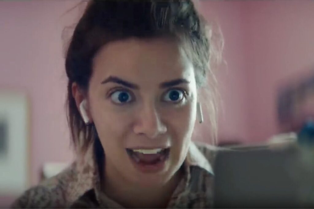 Woman reacting with wide eyes during a virtual meeting in Apple’s remote work ad, illustrating the humor of work-from-home struggles.
